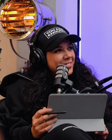 Rutu King-Stubbs at the podcast microphone in headphones and a You Are Enough cap